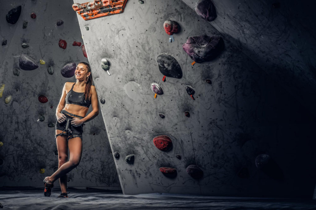 young sporty woman climbing artificial boulder indoors